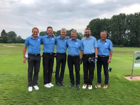 Herren-Golfteam in blauen Poloshirts posiert lächelnd auf dem Fairway, Gruppenfoto beim Turnier.