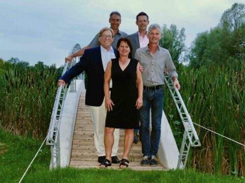Mitarbeiter-Teamfoto auf Holzbrücke im Park: fünf Personen posieren im Sommer vor Schilf, Naturhintergrund