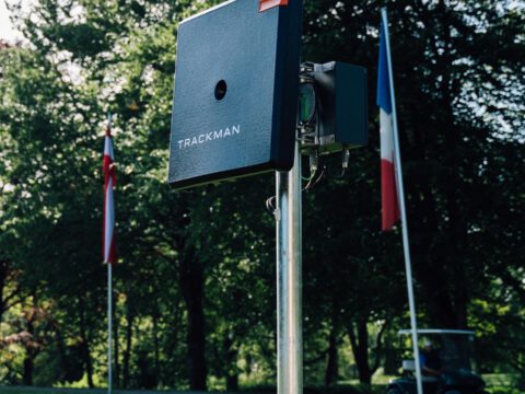 TrackMan Launch Monitor auf dem Golfplatz – Radar zur Schlaganalyse, neben Fahnen und Golfcart im Hintergrund