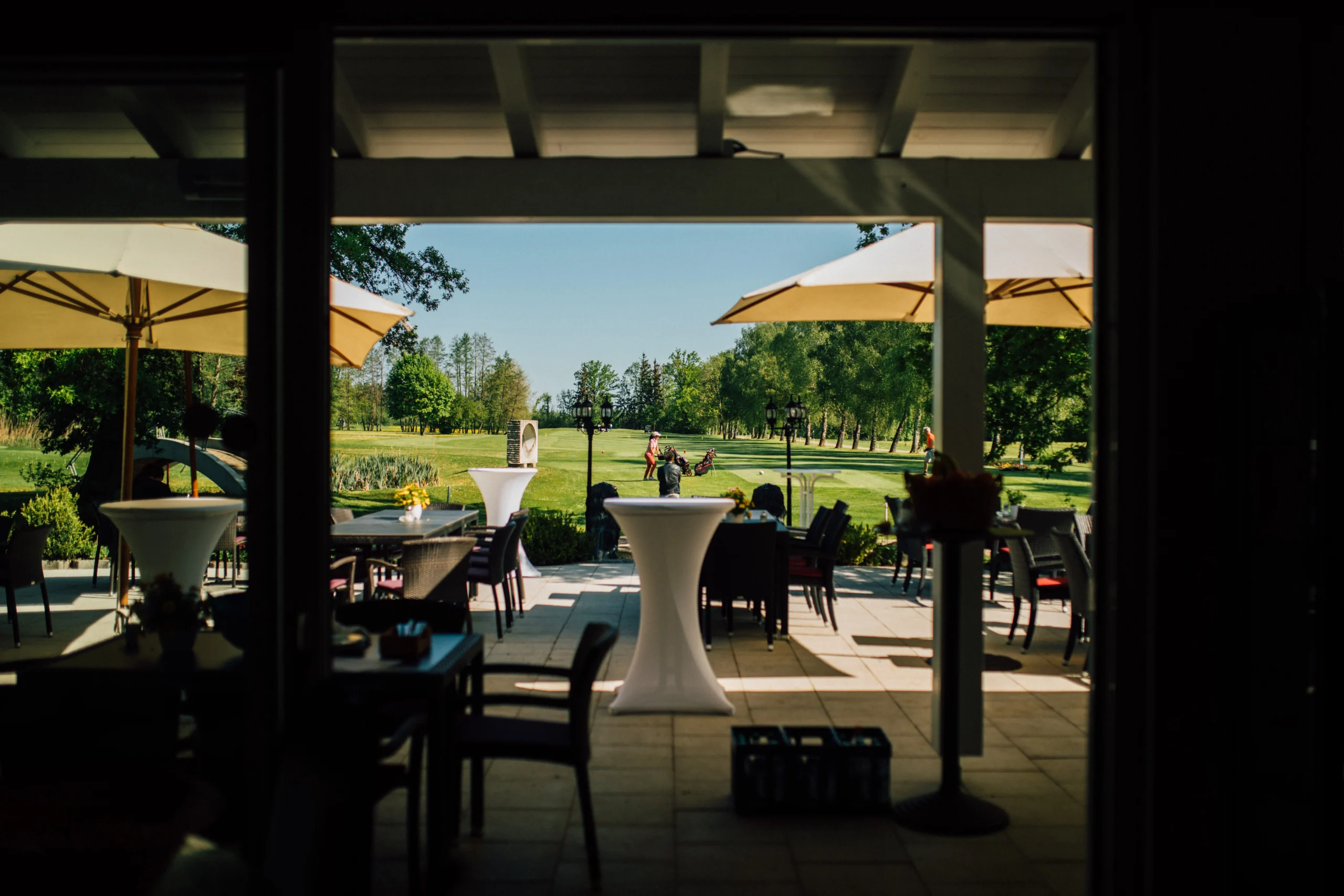 Sonnenterrasse mit Schirmen am Golfplatz: Restaurantblick aufs Green, Tische im Schatten, Naturidylle für Events